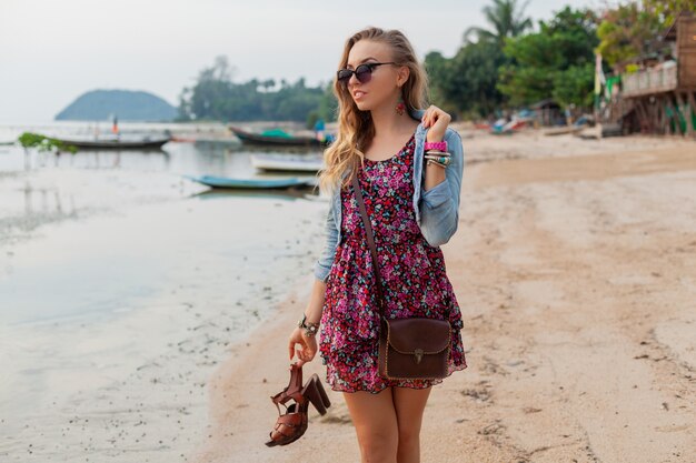 Mulher elegante com vestido de verão, caminhando na praia com sapatos na mão