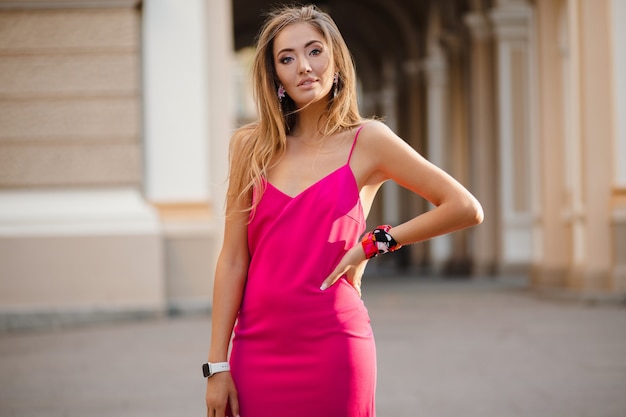Mulher elegante e atraente usando um vestido rosa sexy de verão andando na rua segurando uma bolsa