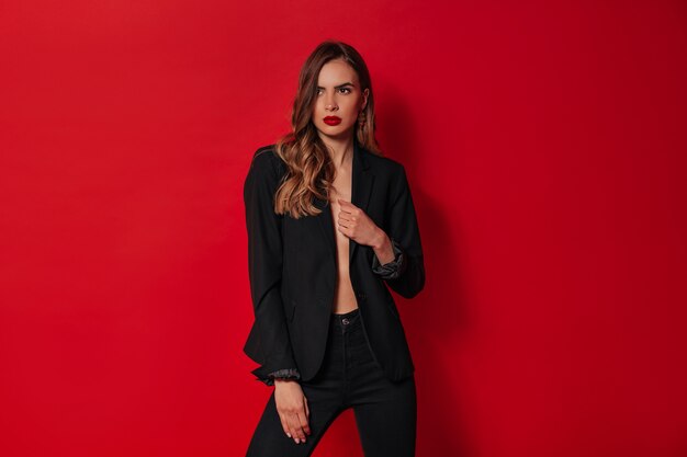 Mulher elegante e confiante em roupa preta posando sobre uma parede vermelha