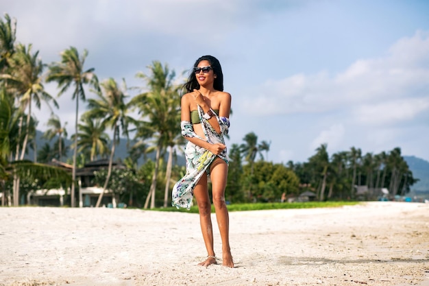 Mulher elegante elegante posando na praia exótica tropical, férias de luxo, usando óculos de sol de biquíni e roupas de praia. Foto Premium