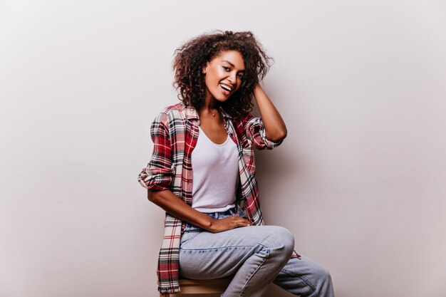 Mulher elegante em jeans vintage azul sorrindo. Menina africana elegante em traje casual, desfrutando de um ensaio fotográfico.