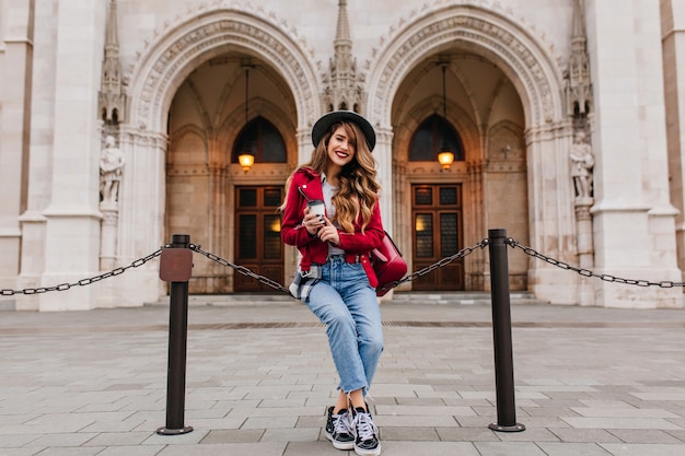 Foto grátis mulher elegante em roupas casuais expressando emoções sinceras enquanto posa perto de um lugar histórico