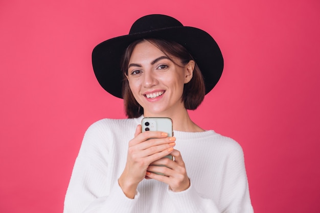 Mulher elegante em suéter branco casual e chapéu na parede rosa vermelha