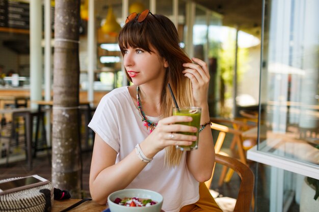 Mulher elegante feliz comendo comida saudável, sentado no belo interior com flores verdes