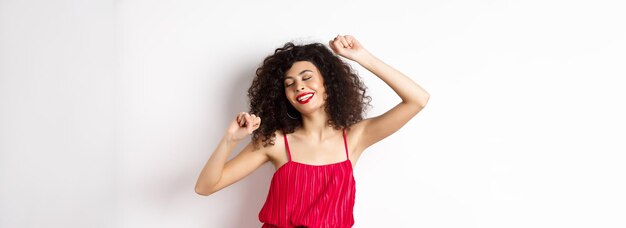 Mulher elegante feliz no vestido vermelho dançando no fundo branco do estúdio