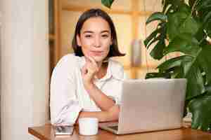 Foto grátis mulher elegante jovem confiante com laptop sentado no café e trabalhando como freelancer no espaço de coworking