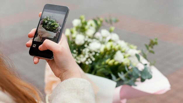 Mulher elegante na cidade tirando foto de um buquê de flores