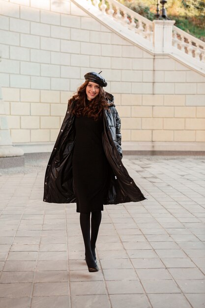 Mulher elegante posando no inverno outono tendência da moda casaco baiacu preto e boina com chapéu de couro na antiga e bonita rua usando sapatos de salto alto
