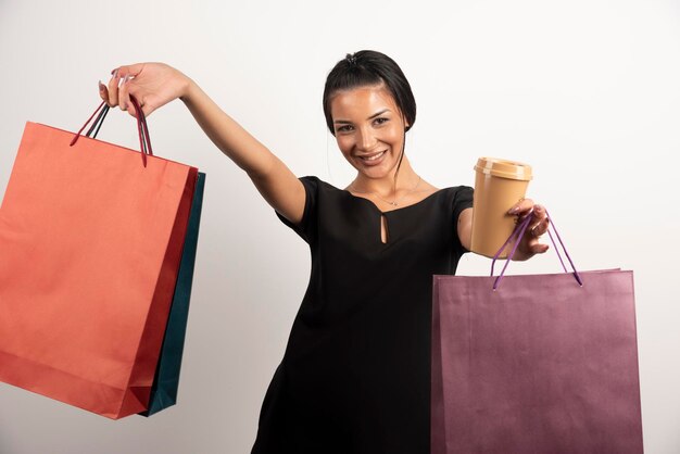 Mulher elegante segurando um monte de sacolas de compras e uma xícara de café.