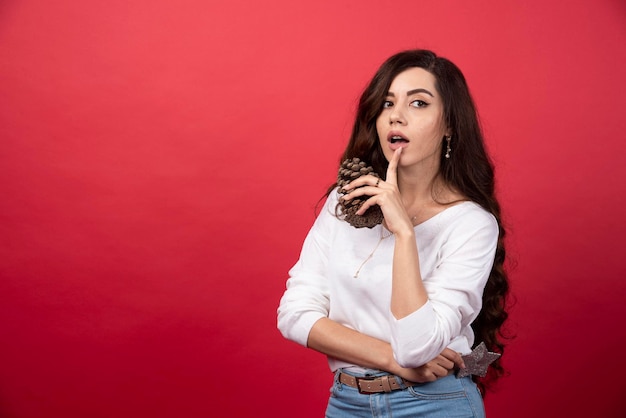 Mulher elegante segurando uma grande pinha de Natal sobre fundo vermelho. Foto de alta qualidade