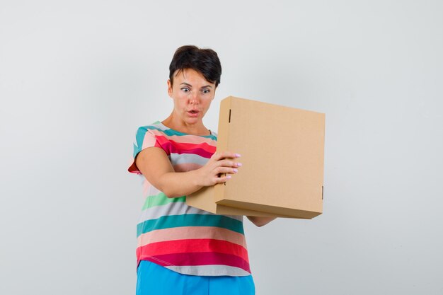 Mulher em camiseta listrada, calça olhando para uma caixa de papelão e parecendo maravilhada