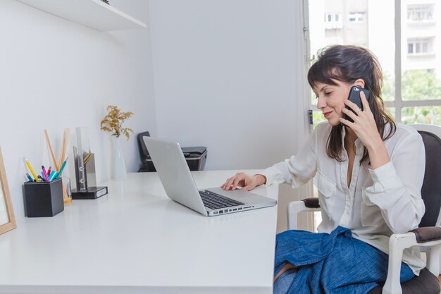 Mulher em casa com laptop falando ao telefone