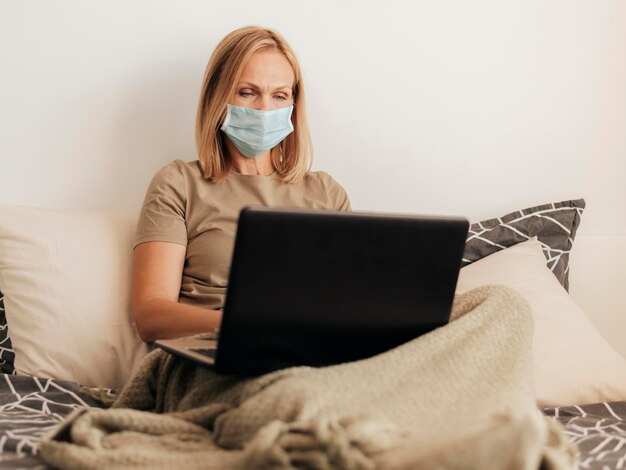 Mulher em casa com máscara médica e laptop