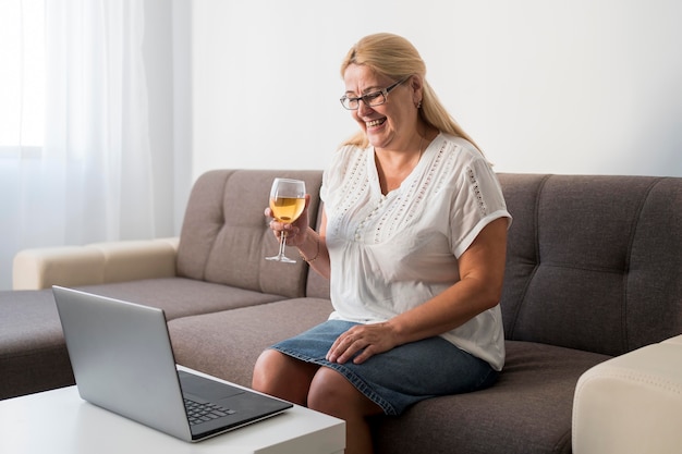 Mulher em casa em quarentena fazendo uma videochamada no laptop com bebida