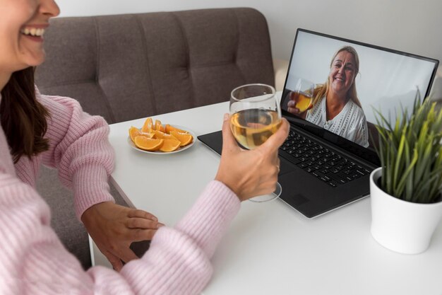 Mulher em casa em quarentena tomando uma bebida com um amigo no laptop