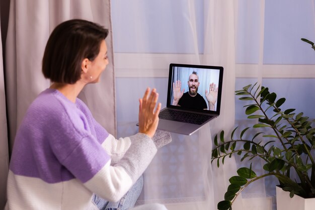 Mulher em casa fazendo videochamadas com os amigos, marido e namorado, conversando on-line em um laptop