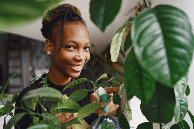 Mulher em casa. Rapariga com uma camisola preta. Mulher africana usa o pano. Pessoa com vaso de flores.