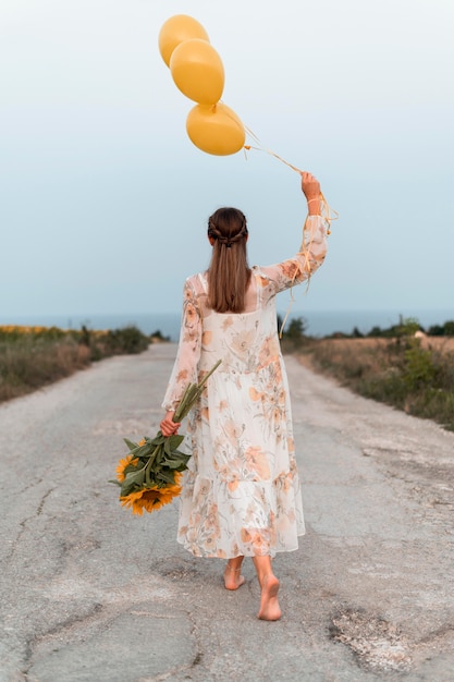 Mulher em cena completa segurando balões e flores
