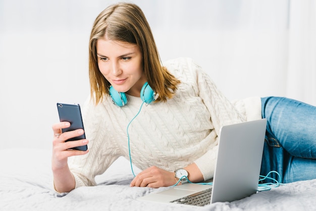 Mulher em fones de ouvido usando smartphone perto de laptop