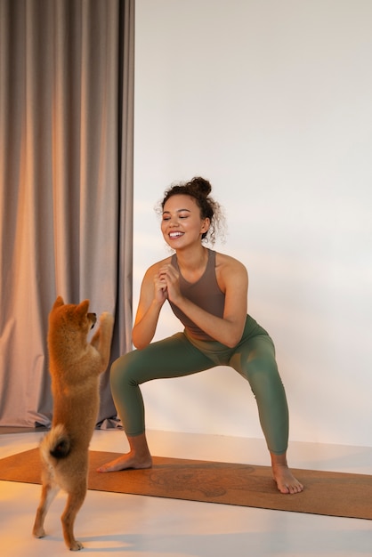 Mulher em forma de tiro completo praticando esporte com cachorro dentro de casa