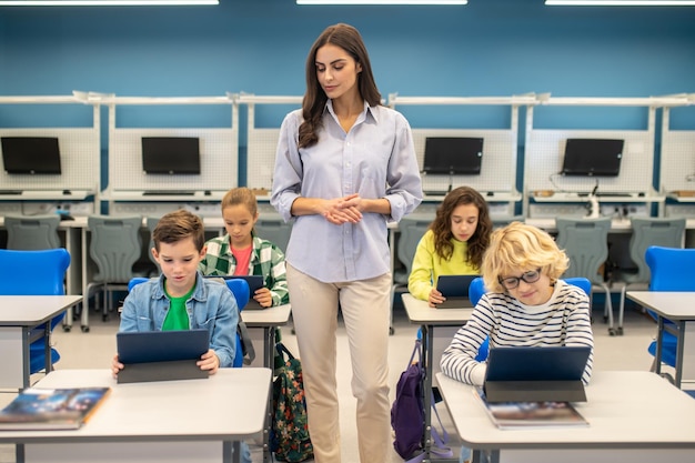 Mulher em pé assistindo alunos trabalhando em tablets