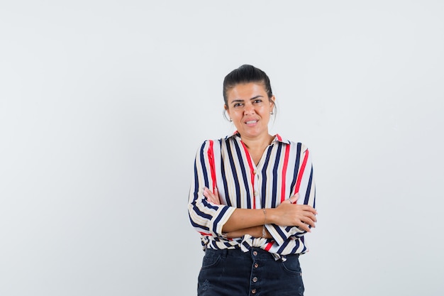 mulher em pé com os braços cruzados na camisa, saia e parecendo confiante.