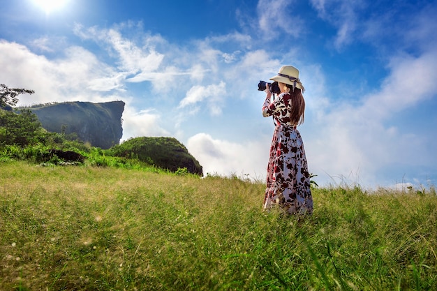 Mulher em pé no prado e segurando a câmera tira uma foto nas montanhas de Phu Chi Fa em Chiangrai, Tailândia. Conceito de viagens.