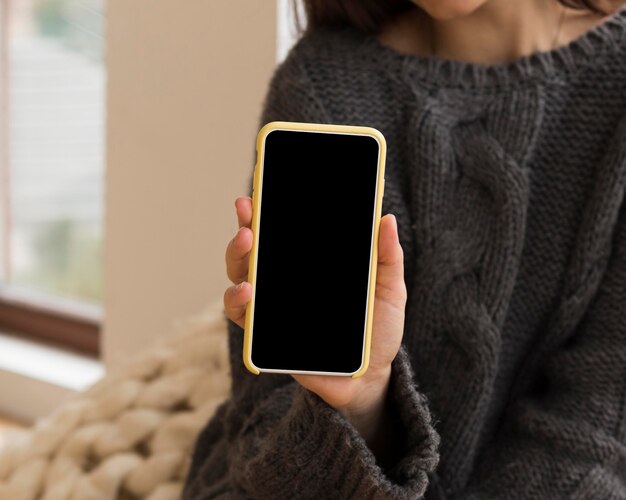 Mulher em roupas confortáveis segurando um telefone em branco