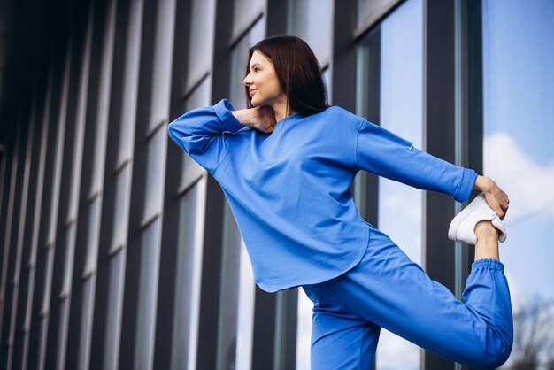 Mulher em roupas esportivas azuis, estendendo-se para fora da rua