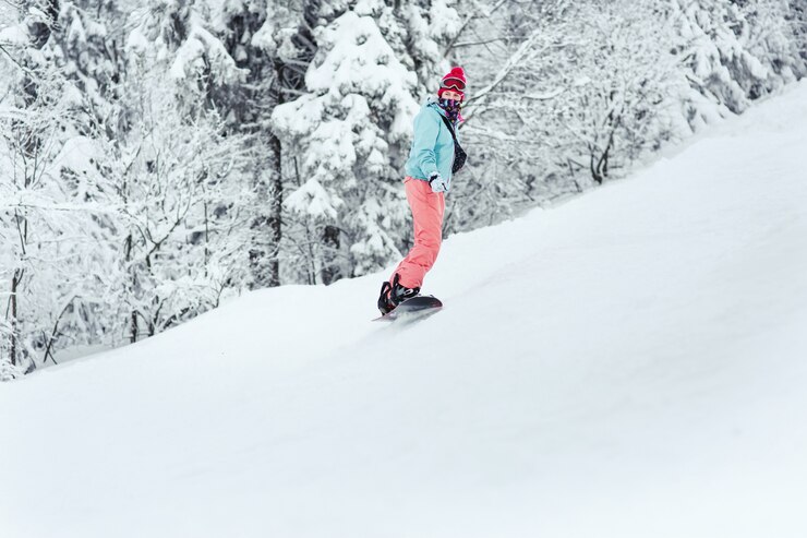 Foto grátis mulher em terno de esqui olha por cima do ombro descendo a colina em seu snowboard