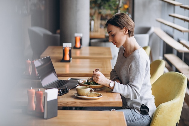 Mulher em um café almoçando e falando no telefone