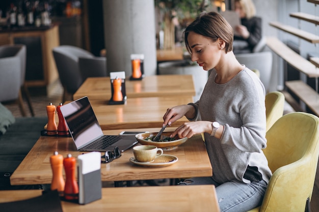 Mulher em um café almoçando e falando no telefone