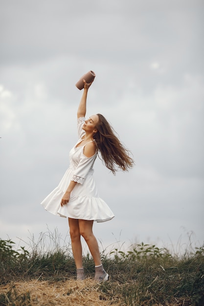 Mulher em um campo de verão. Morena em um vestido branco. Menina com alto-falante de música.