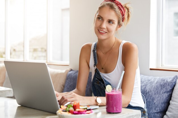 Mulher em um macacão jeans elegante com laptop na cafeteria