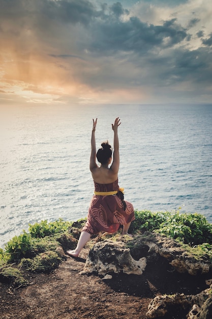 Mulher em um penhasco com vista para o mar saudando o sol