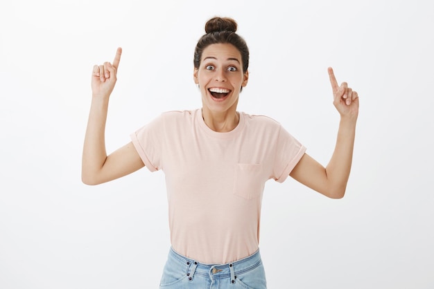 Foto grátis mulher em uma camiseta casual levantando as mãos para apontar sorrindo animada, alegre por reagir à incrível surpresa inesperada na parede cinza.