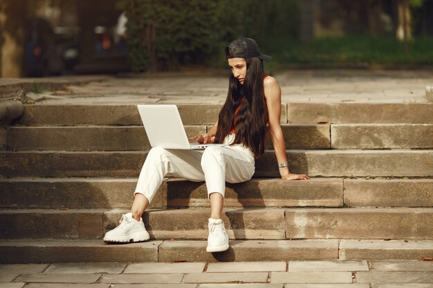 Mulher em uma cidade de primavera. Senhora com um laptop. Menina sentada em uma escada.