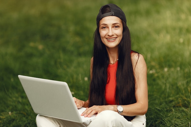 Mulher em uma cidade de primavera. Senhora com um laptop. Menina sentada na grama.