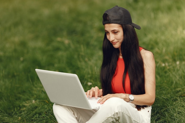 Mulher em uma cidade de primavera. Senhora com um laptop. Menina sentada na grama.