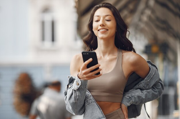 Mulher em uma cidade de verão. Senhora com telefone. Morena perto do prédio.