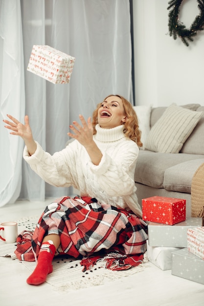 Mulher em uma sala. Loira com um suéter branco. Senhora perto da árvore de Natal.