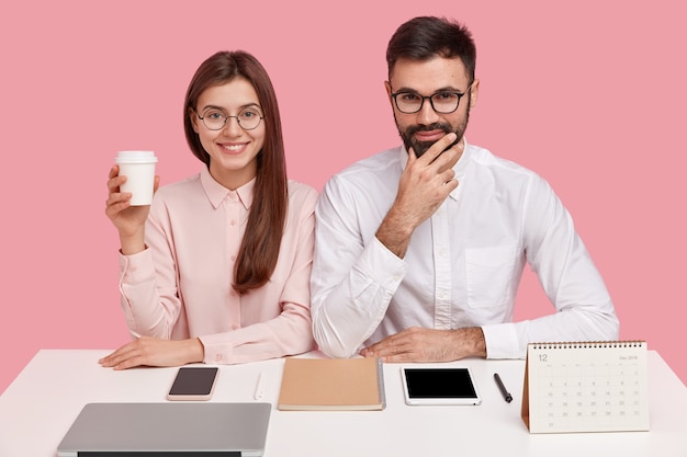 Foto grátis mulher encantada tem sorriso cheio de dentes, usa óculos ópticos, segura café para viagem, tem expressão satisfeita