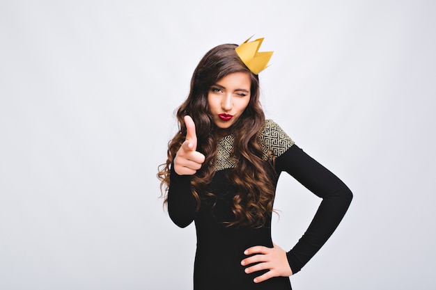 Mulher encantadora animada na coroa amarela se divertindo. Mulher brincalhona, vestido de moda elegante, emoções sérias. Festa de ano novo, comemoração de feriados, aniversário, brincar.