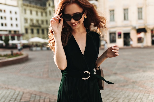 Foto grátis mulher encantadora com roupa de veludo e óculos escuros sorrindo lá fora