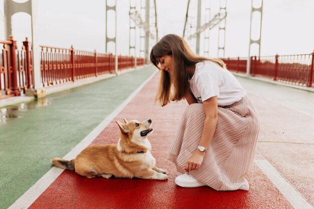 Mulher encantadora de saia rosa e camiseta branca treinando com seu cachorro lá fora