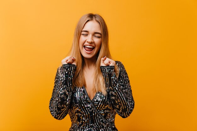 Mulher encantadora e elegante, expressando felicidade e sorrindo. Mulher bonita positiva em uma jaqueta brilhante em pé na laranja