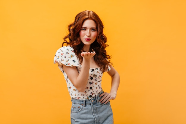 Mulher encantadora em saia jeans e top com flores sopra beijo no fundo isolado.