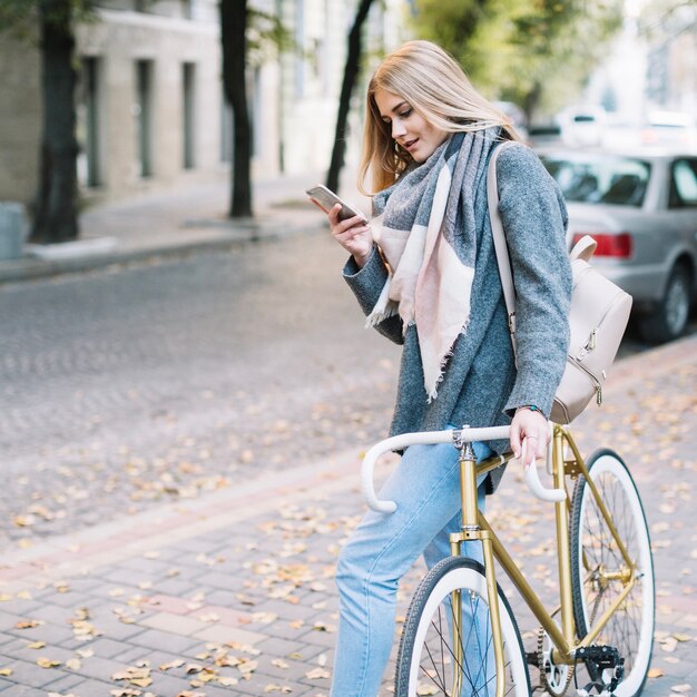Mulher encantadora que procura o telefone perto da bicicleta