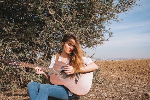 Mulher encantadora tocando violão perto do arbusto