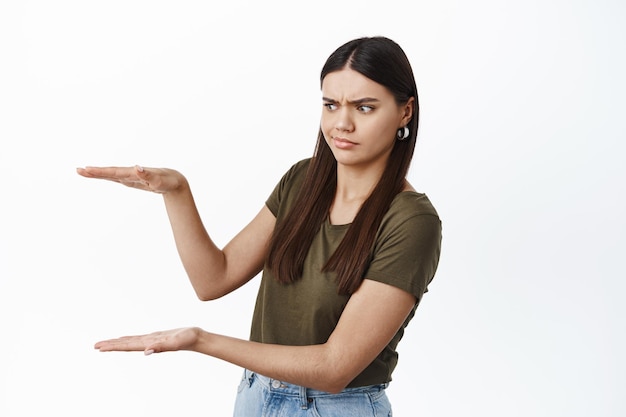 Foto grátis mulher encara confusa as mãos segurando o espaço da cópia, olhando para o gesto de caixa vazia como se estivesse carregando um produto nas mãos